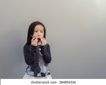 Little Asian Child Play The Harmonica, Gray Background