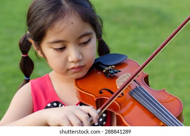 Little Asian Child Playing Violin In The Park