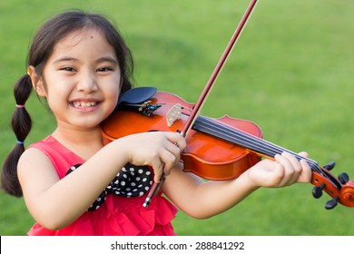 Little Asian Child Playing Violin In The Park