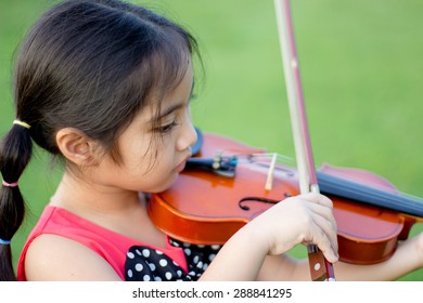 Little Asian Child Playing Violin In The Park