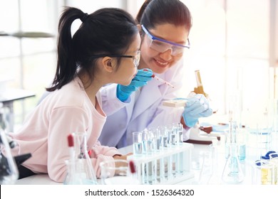 little asian children girl in elementary science class book doing chemical experiment helped by woman teacher test, experimen, try drop color water to plate. Education science workshop concept.