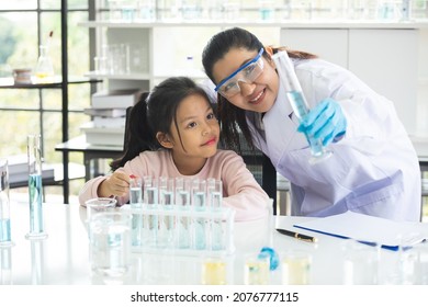 little asian children girl in elementary science class doing chemical experiment helped by woman teacher test, experimen, try drop color water to plate. Education science workshop concept.
