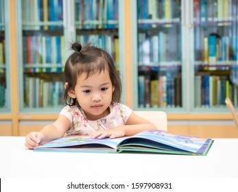 Little Asian Cute Girl 3-4 Years Old Sitting On Chair And Looking A Kid's Book At The Library. Learning And Education Of Kid.