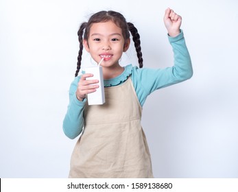 Little Asian Cute Girl 6 Years Old Holding And Drinking Milk From Carton Of Milk With Rise One Hand Up Over White Background. Milks Is Essential And Nutrition For The Child's Body.