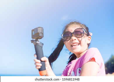 Little asian girl child holding action camera and recording video at the sea beach with sun light flare.Photographer kid girl smiling and happy when she take a photo with action cam video in vacation. - Powered by Shutterstock