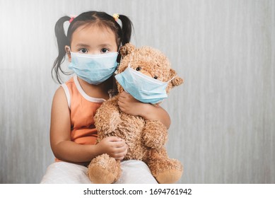 Little Asian Girl Child Holding A Teddy Bear Wearing A Mask. Concept Of Pediatric Health Care And Infection