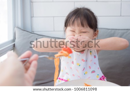 Little asian girl close her mouth by hands,refuse to eat tomato in spagethi from her mother.Picky eater child concept.