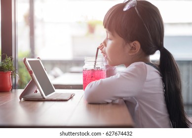 Little Asian Girl Drinking Red Water In Breakfast Time. See The IPad