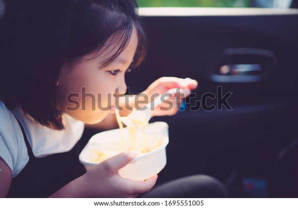 Little asian girl enjoy eating with go box\
set spaghetti bolognese with cheese on go box in the car.Delivery\
service,Takeaway, Food delivery and Stay at home safe lives from\
Covid-19 Coronavirus.