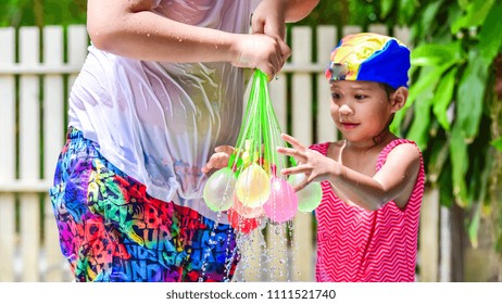 A Little Asian Girl Funny Playing Colorful Water Balloon On Her Hand In Plastic Swimming Pool.