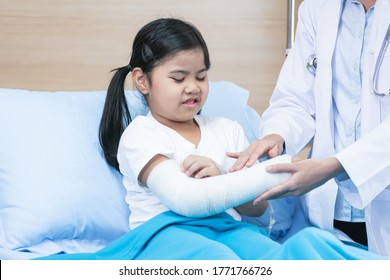 A little asian girl getting hurt while wearing a cast on her broken arm. She staing on bed in hospital. Health, Insurance and Medical Concept. - Powered by Shutterstock