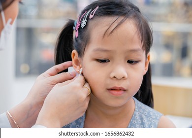 Little Asian Girl Having Ear Piercing Process. Cleaning By Projessional