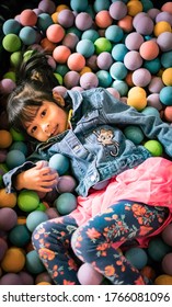 Little Asian Girl Having Fun In Ball Pit With Colorful Balls. Child Playing On Indoor Playground. Kid Jumping In Ball Pool.