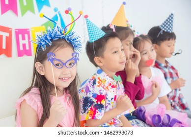 Little Asian Girl Holding Eyeglasses ,party Accessory With Friends At Birthday Party