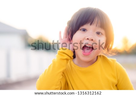 Little asian girl holds her hand near her ear and listening.Disability day.Deaf kid.Exciting face on asian child girl wear yellow shirt in winter time.Turning off phone and listening your child.