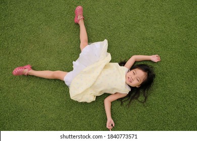 Little Asian Girl Laying Down On The Green Grass Top View