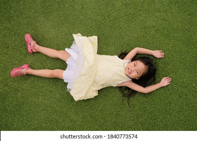 Little Asian Girl Laying Down On The Green Grass Top View