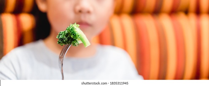 Little Asian Girl Make Vomiting Face When She Eat Broccoli Vegetable In Restaurant.Unhappy, Disgusted, Unlike Veggie Food.Little Asian Girl Child With No Appetite In Front Of The Meal.Bad Behavior.