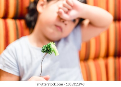 Little Asian Girl Make Vomiting Face When She Eat Broccoli Vegetable In Restaurant.Unhappy, Disgusted, Unlike Veggie Food.Little Asian Girl Child With No Appetite In Front Of The Meal.Bad Behavior.