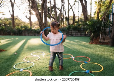 Little Asian Girl Playing Hula Hoop In The Garden