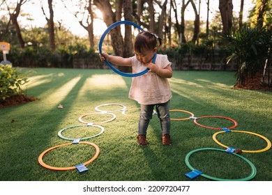 Little Asian Girl Playing Hula Hoop In The Garden