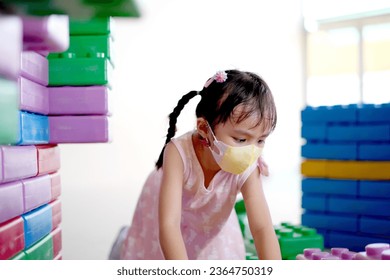 Little asian girl playing indoors building a house with big plastic construction bricks - Shutterstock ID 2364750319