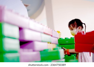 Little asian girl playing indoors building a house with big plastic construction bricks - Shutterstock ID 2364750389