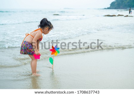 Little asian girl playing on the beach.Young Asian child girl is playing colored pinwheel on the beach.Vacation and relax concept.