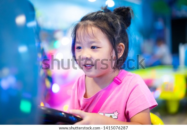 Little asian girl playing Racing car arcade game\
machine in Game center.Kid girl holding steering wheel and playing\
Game.Little girl playing racing simulator game in theme park.E\
sports concept.