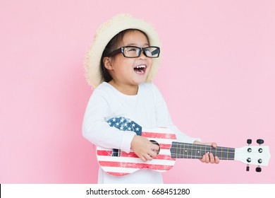 Little asian girl playing ukulele on pink background 