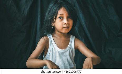 A Little Asian Girl In A Pose Shows An Expression. Portrait Of A Child With A Dark Background. Cinematic Look Picture. Gestures Education Concept.