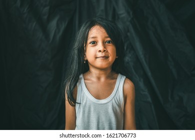 A Little Asian Girl In A Pose Shows An Expression. Portrait Of A Child With A Dark Background. Cinematic Look Picture. Gestures Education Concept.