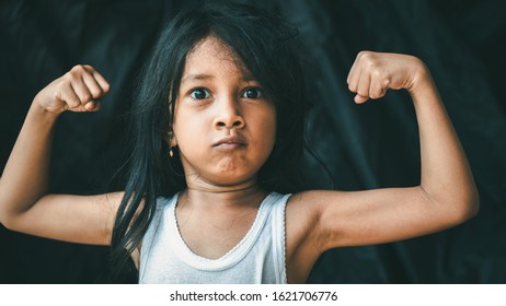 A Little Asian Girl In A Pose Shows An Expression. Portrait Of A Child With A Dark Background. Cinematic Look Picture. Gestures Education Concept.