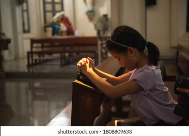 Little Asian Girl With Praying At Christ Church. Kid Asia Girl Closed Her Eyes, Praying To Peace With Scripture Bible. People Hope, Dreams Concept.