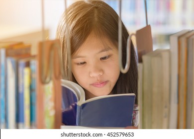 Little Asian Girl Reading A Book In Library At School