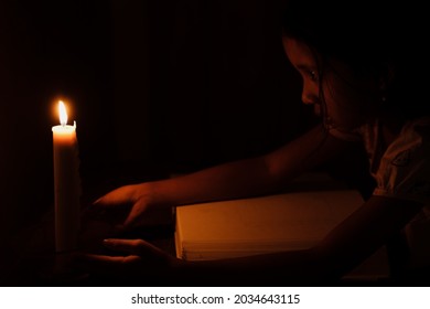 Little Asian girl is reading in a dark room lit only by candlelight. The concept of children's education in a village without electricity.