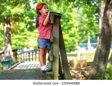 Little Asian Girl Singing Outside. Small Female Child Screaming Outdoors. Small Asian Kid Being Silly At The Park Standing On A Bridge Being Really Loud During The Summertime.