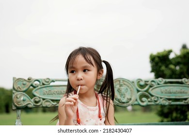 Little asian girl sits in the garden and holds a  biscuit bread sticks in his hand. Copy space.