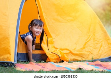 Little Asian girl smile and looking at camera playing with her tent on campsite, happy girl sitting inside yellow tent at park - Powered by Shutterstock