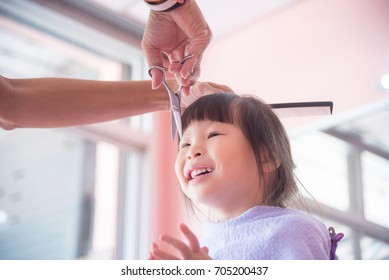 Little asian girl smiling while hairdresser cutting her hair