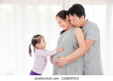 Little asian girl touching her pregnant mother belly and smiles