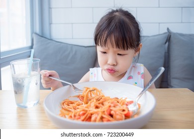 Little Asian Girl With Unhappy Face While Having Fried Spaghetti With Tomato Sauce For Lunch ,picky Eater Child Concept.