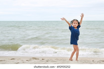 Little Asian Girl Waving Her Hand Saying Goodbye On The Beach.