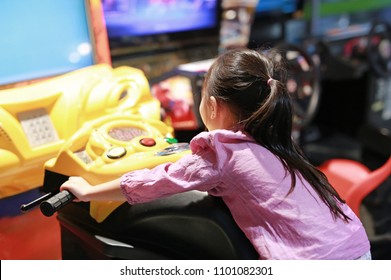 Little Asian kid girl playing arcade video game. Motorcycle Racing.