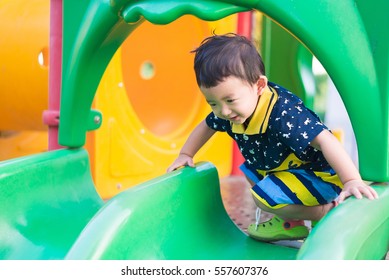 Little Asian Kid Playing Slide At The Playground Under The Sunlight In Summer, Kids Play On School Yard. Happy Kid In Preschool. Shallow DOF