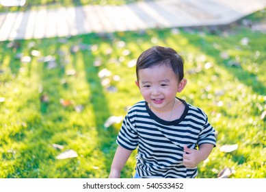 Little Asian Kid Playing And Smiling At The Playground Under The Sunlight In Summer, Kids Play On School Yard. Happy Kid In Kindergarten Or Preschool. Shallow DOF