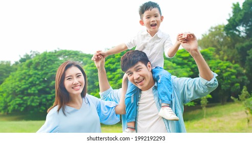 little asian kid sit on father shoulder and smile at you happily in the park