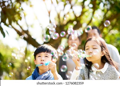 little asian kids boy and girl sister and brother blowing bubbles in a park with parents watching from behind. - Powered by Shutterstock