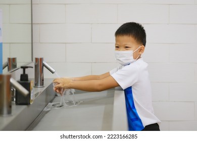 Little Asian student kid wearing medical face mask washing hands by himself on sink  in the basin, bathroom sink and water drop from faucet in public toilet, Clean school washrooms, Selective focus