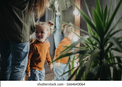 Little Attractive Girl Of 2 Years Is Playing Near The Mirror Next To Her Mom Who Is Applying Makeup, The Baby Is Watching Her Mom Posing In Front Of A Mirror